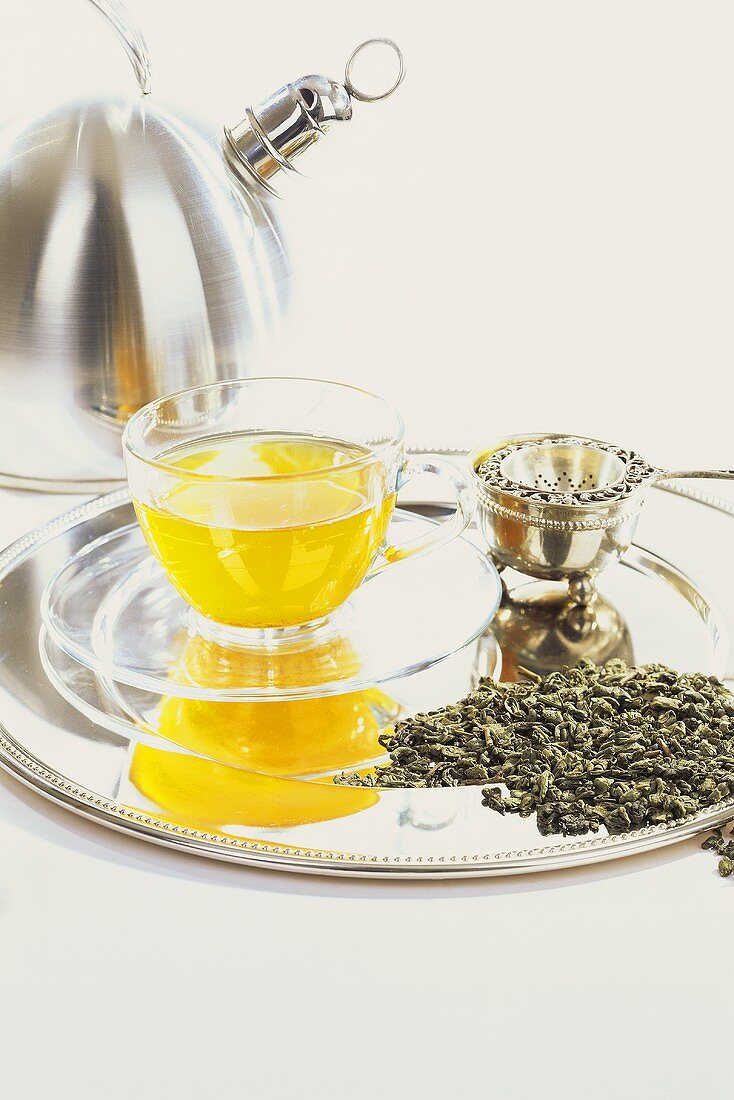 Grüner Tee in Tasse & Teeblätter, dahinter Teekanne