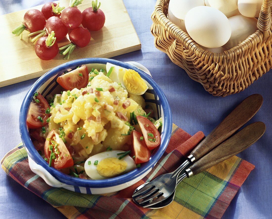 Potato salad with fried bacon cubes, eggs & tomatoes
