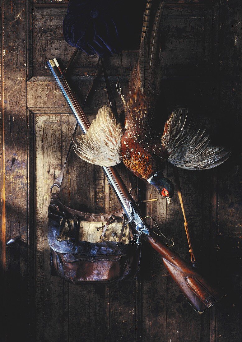 Still life with dead pheasant, leather bag and rifle
