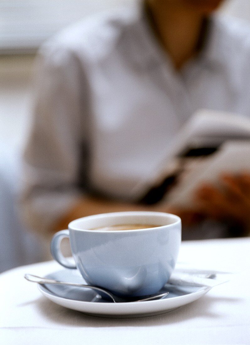 A cup of cappuccino, model with magazine behind