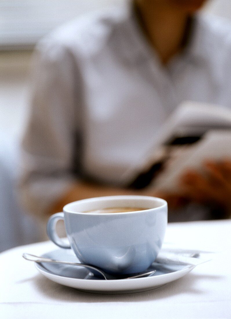 Eine Tasse Cappuccino, dahinter Modell mit Zeitschrift