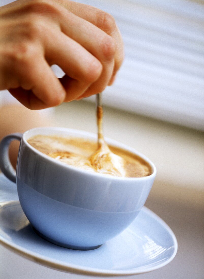 Stirring cappuccino in pale-blue cup