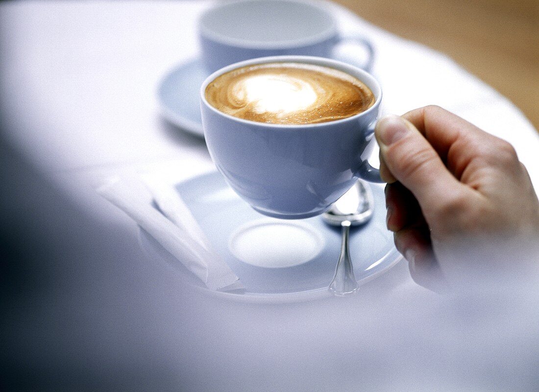 Hand hält Cappuccino in hellblauer Tasse