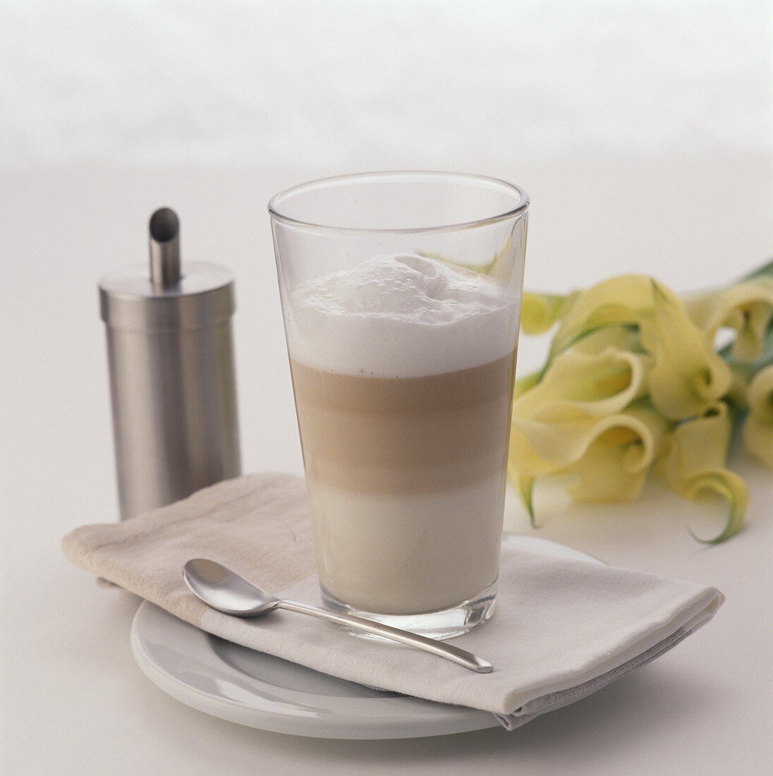 Ein Glas Latte Macchiato vor einem Zuckerstreuer