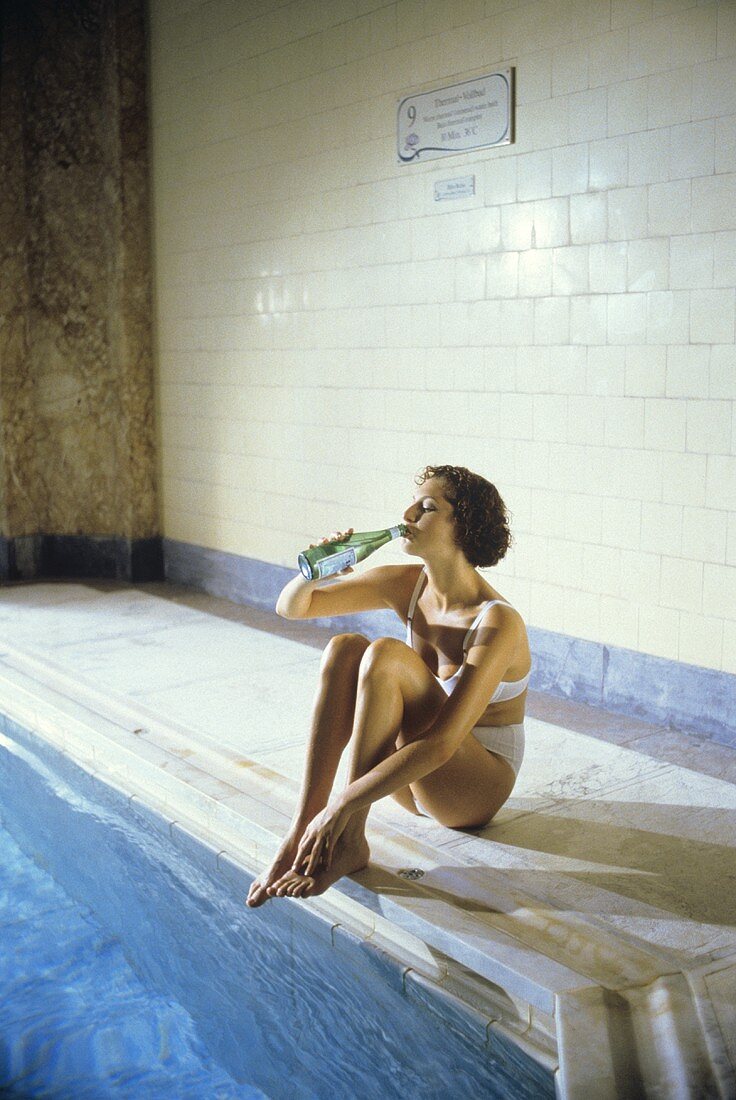 Junge Frau trinkt Wasser aus Flasche am Schwimmbecken