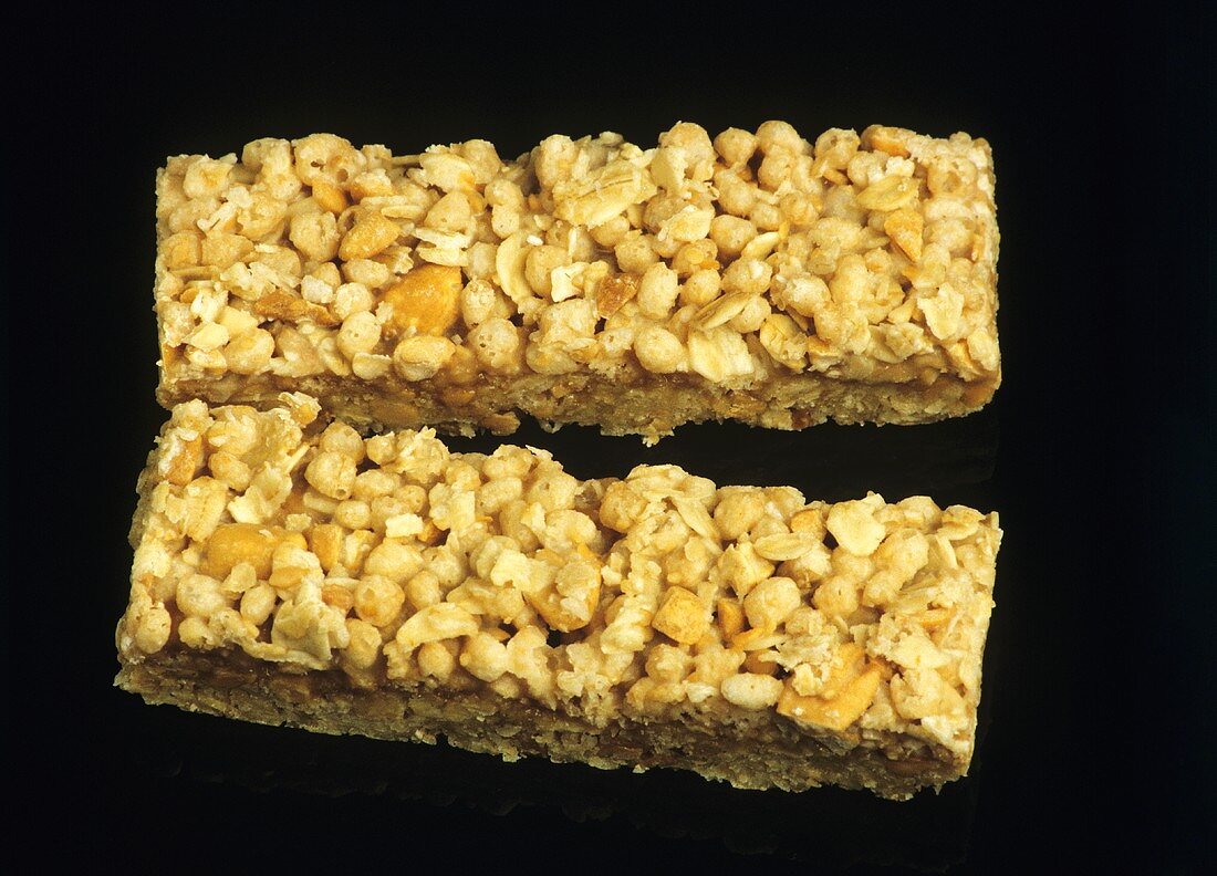Two muesli bars with nuts against black backdrop