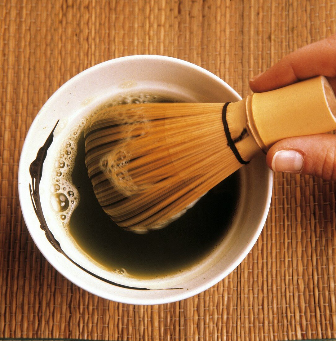 Beating Matcha powder and water with bamboo whisk