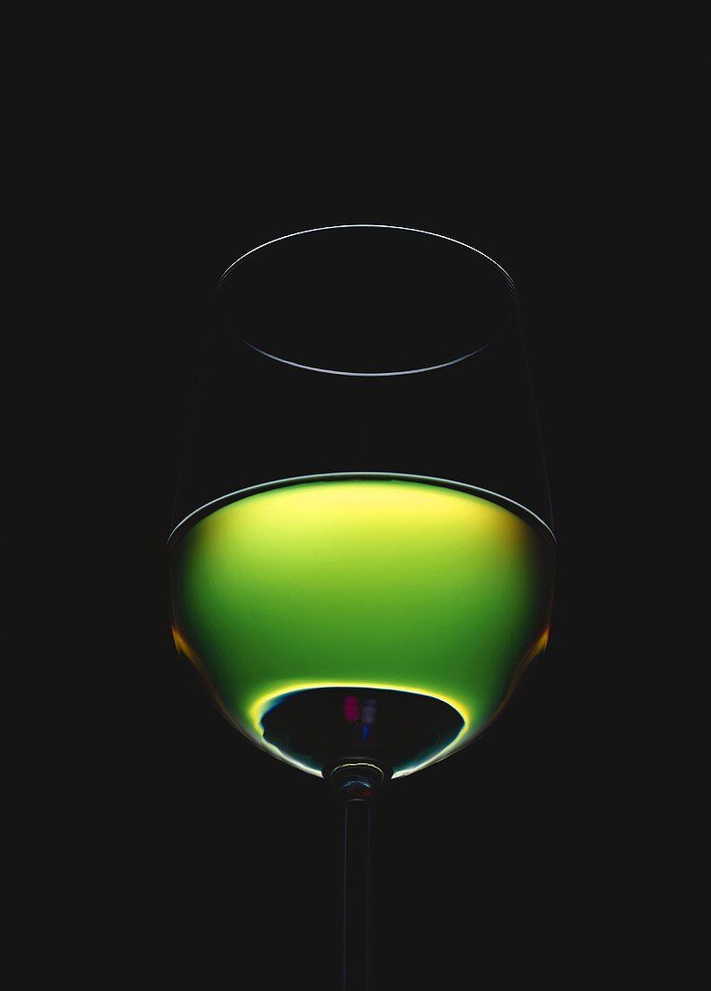 Gefülltes Weissweinglas vor grünem Licht