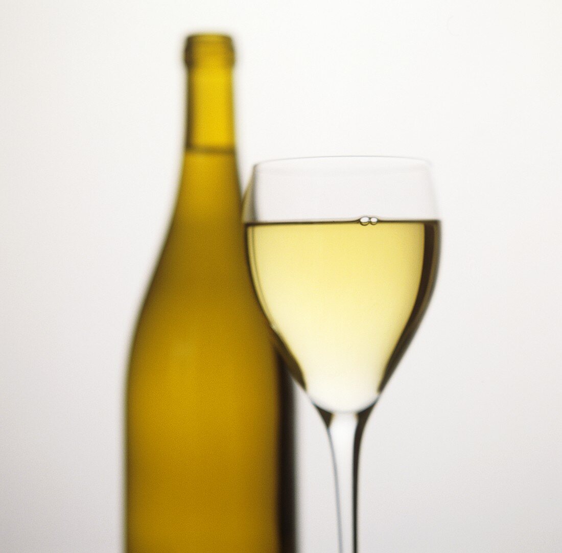 White wine glass in front of unlabelled white wine bottle