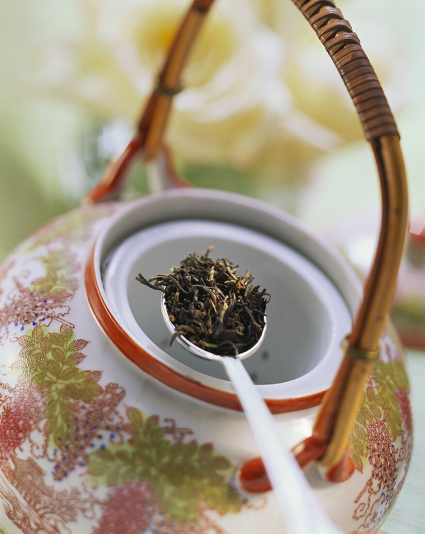 Black tea on spoon above Asian teapot