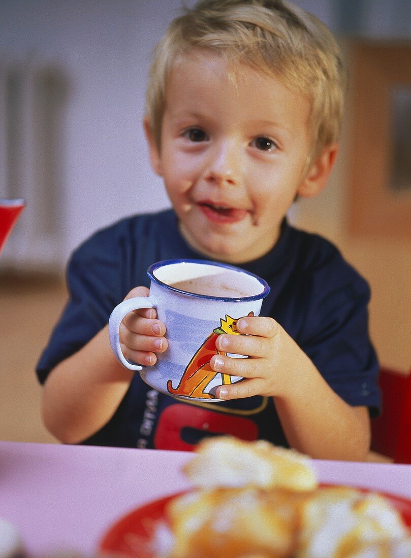 Kleiner Junge mit Gebäck und einem Becher Kakao