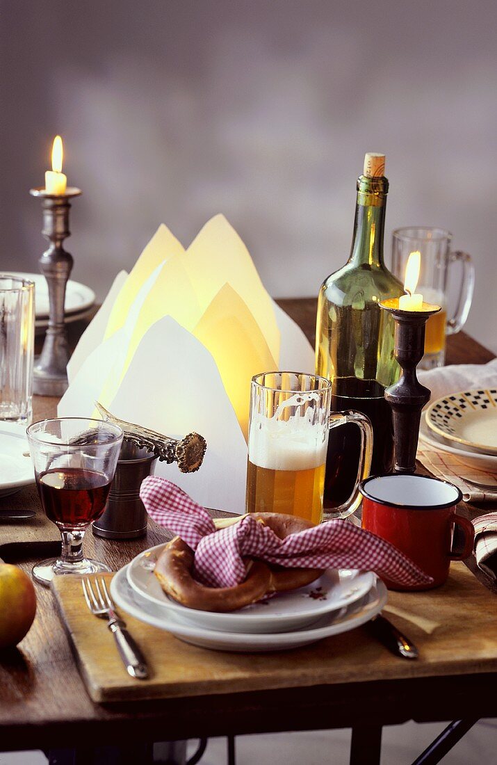 Rustikal gedeckter Tisch mit Brezel, Bier, Wein und Kerzen