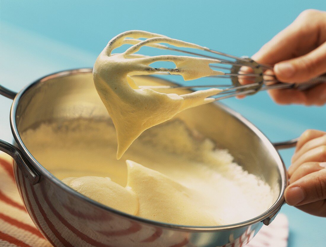 Whisk with sponge mixture above a bowl of sponge mixture