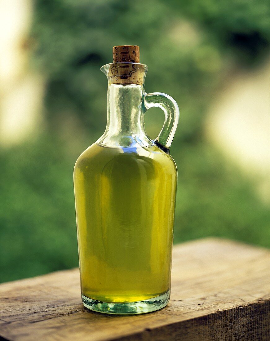 Olive oil in bottle with handles & cork on a wooden board