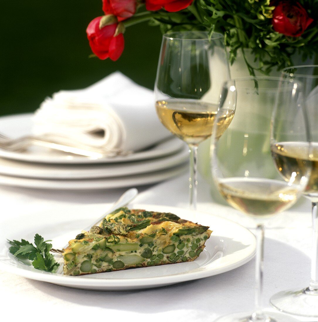 A piece of vegetable frittata on plate, wine glasses