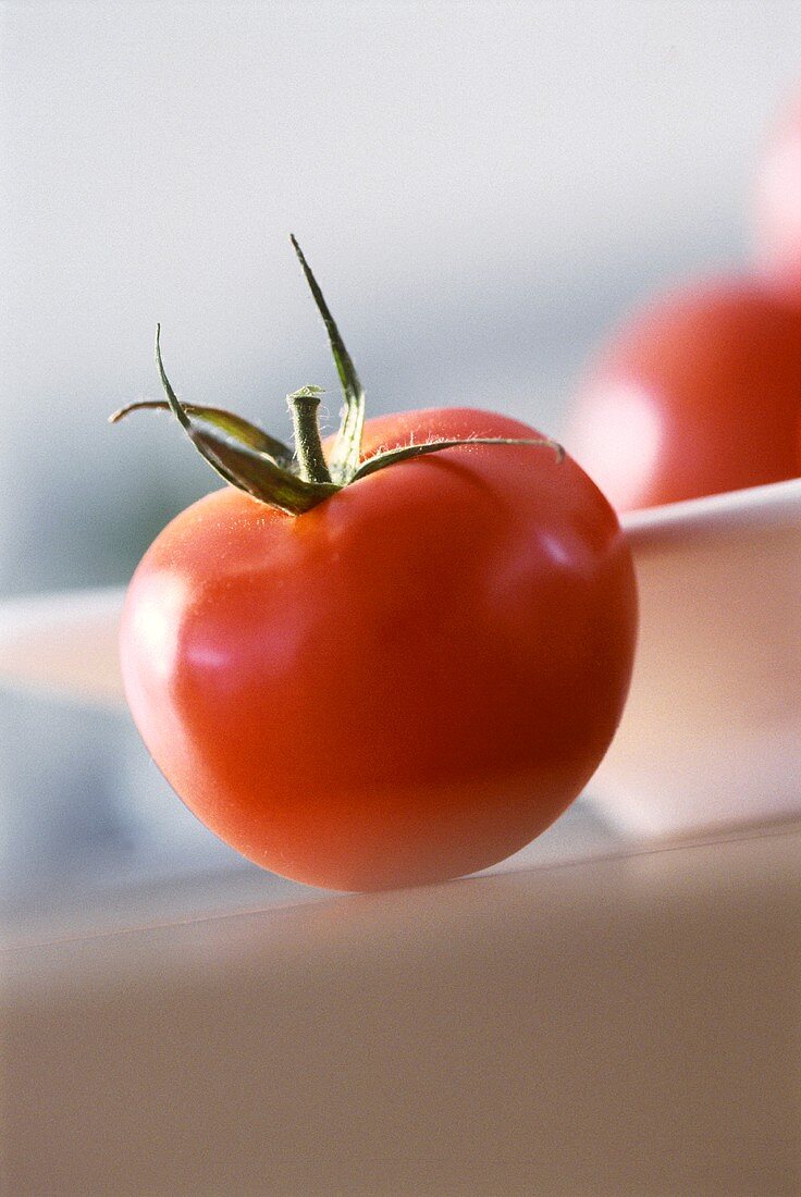 Eine Tomate, dahinter Schüssel mit Tomaten