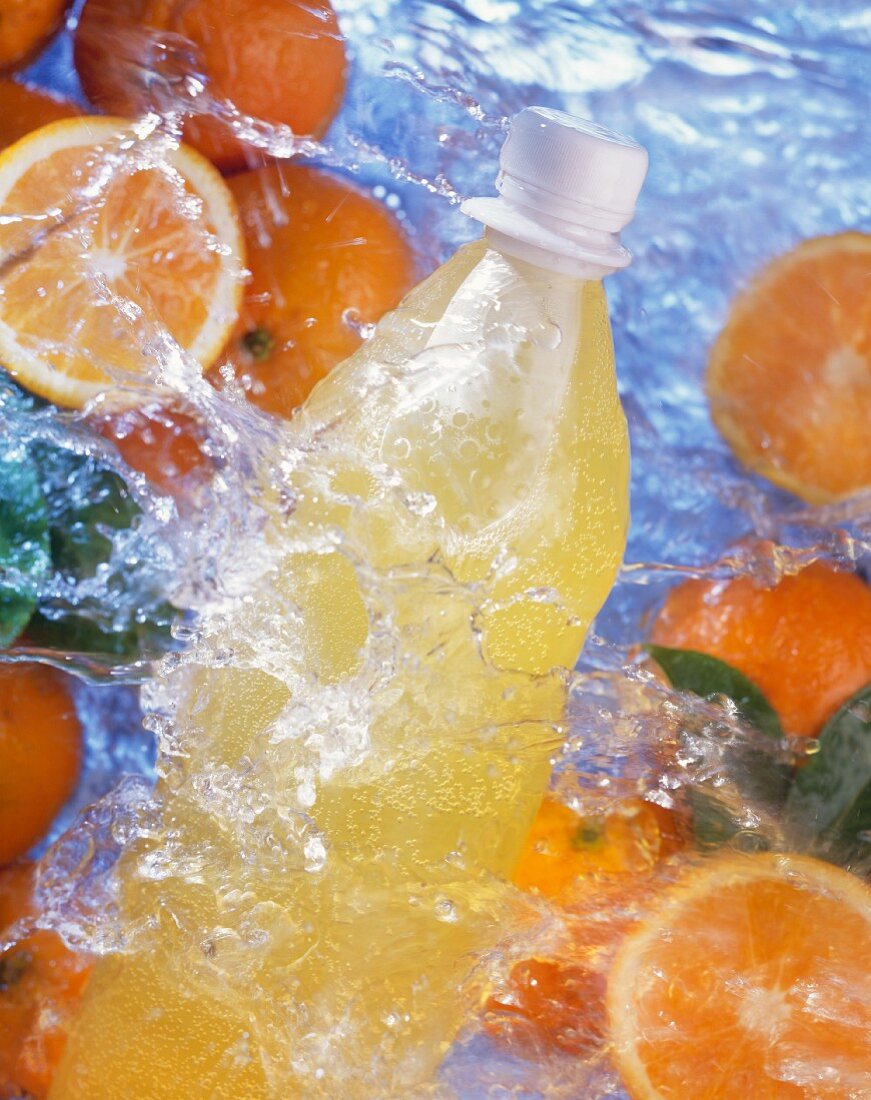 Flasche Orangenlimonade und Orangen im spritzenden Wasser