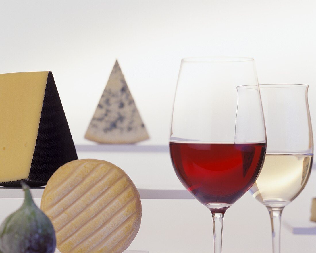 Various types of cheese, two glasses of wine and a fig
