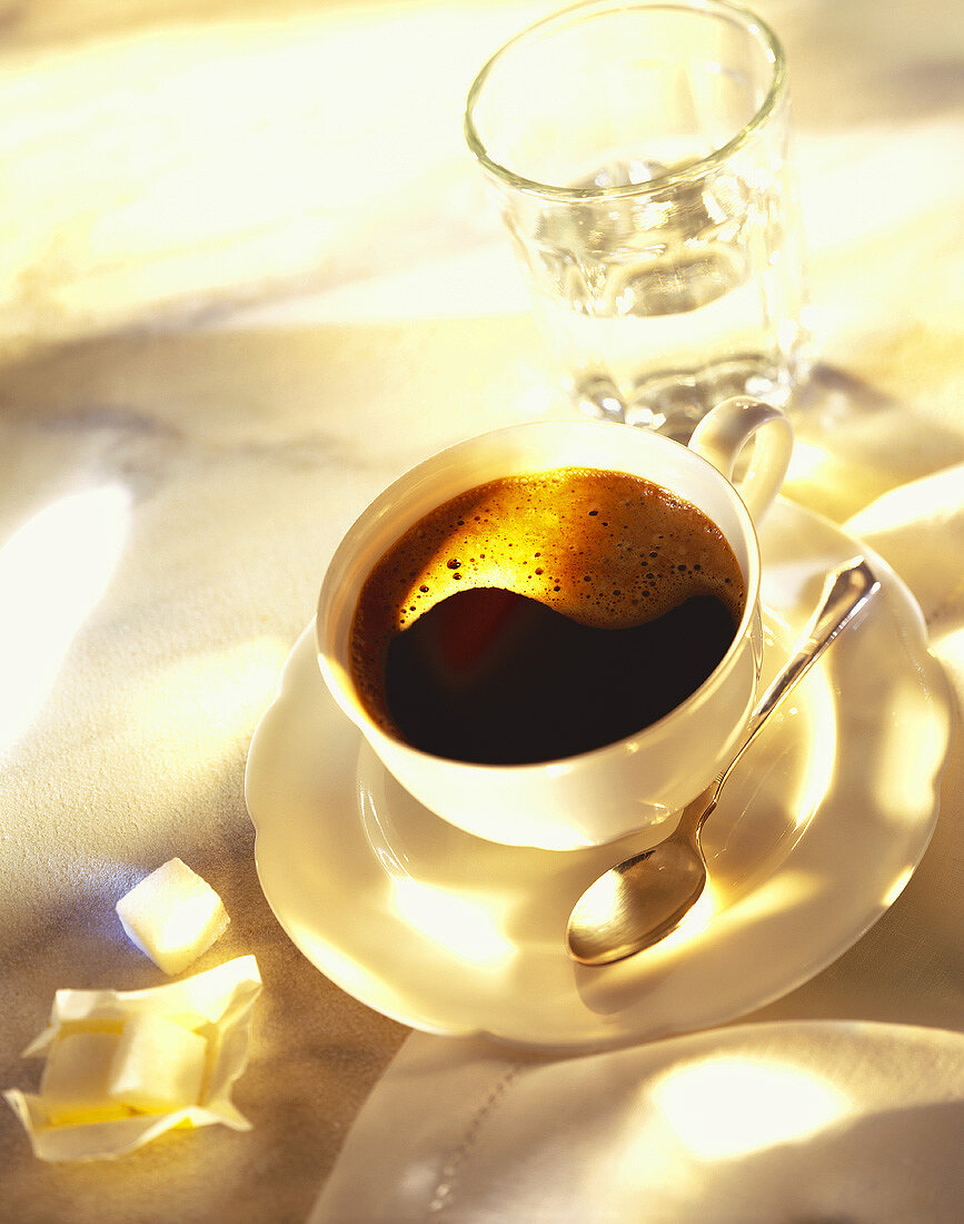 Tasse schwarzer Kaffee, Glas Wasser und Würfelzucker