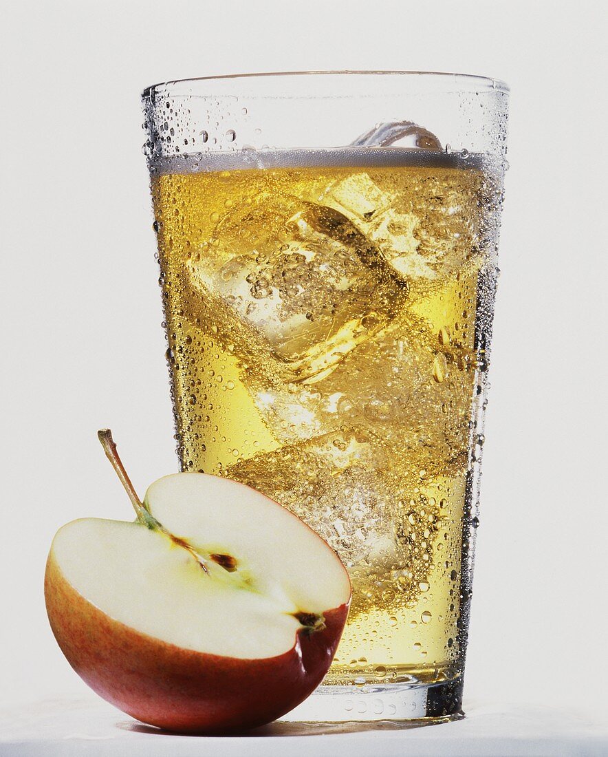 Apple juice drink with ice cubes, half an apple in front