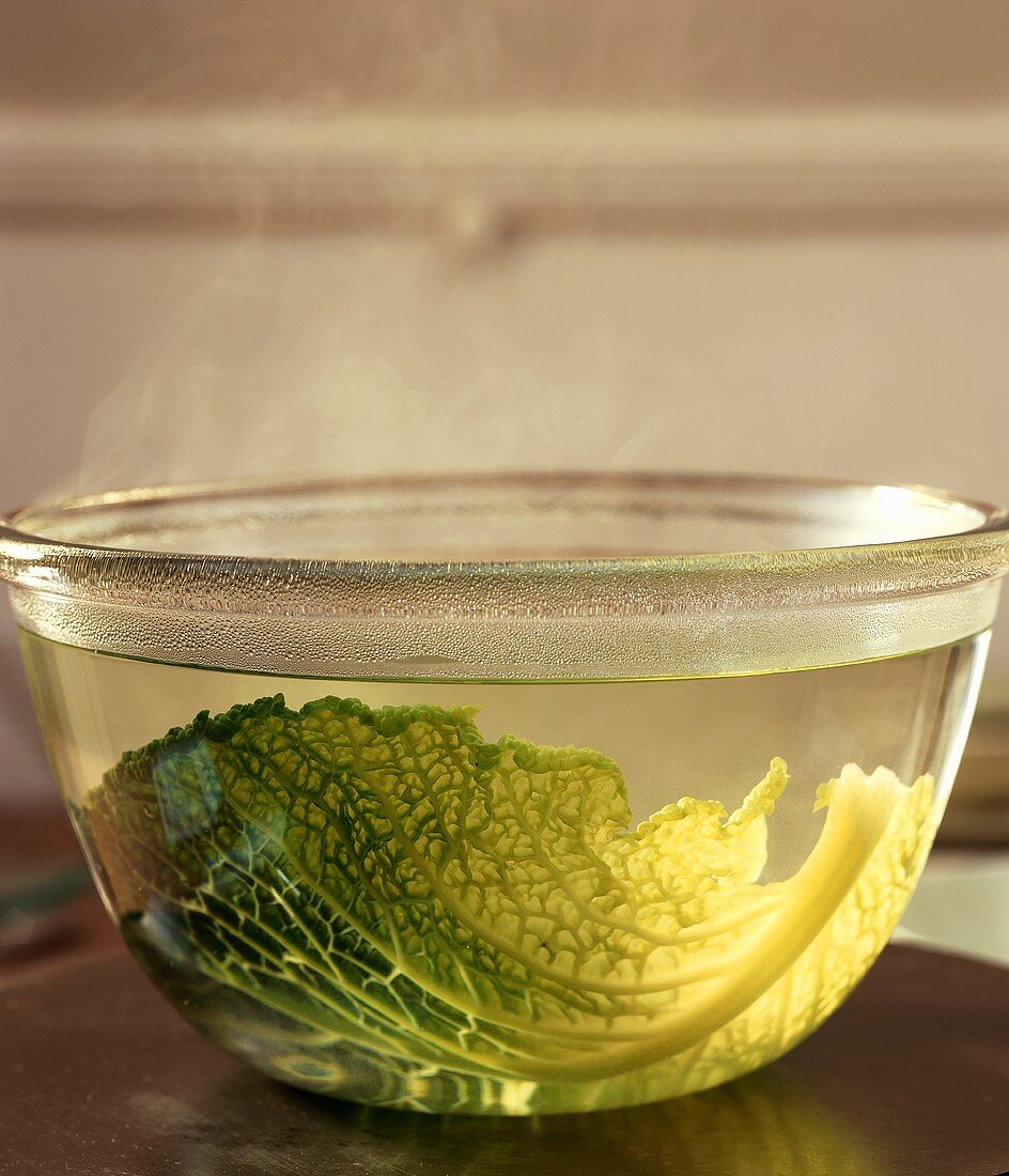 Wirsingkohlblatt in einer Schale mit dampfendem Wasser