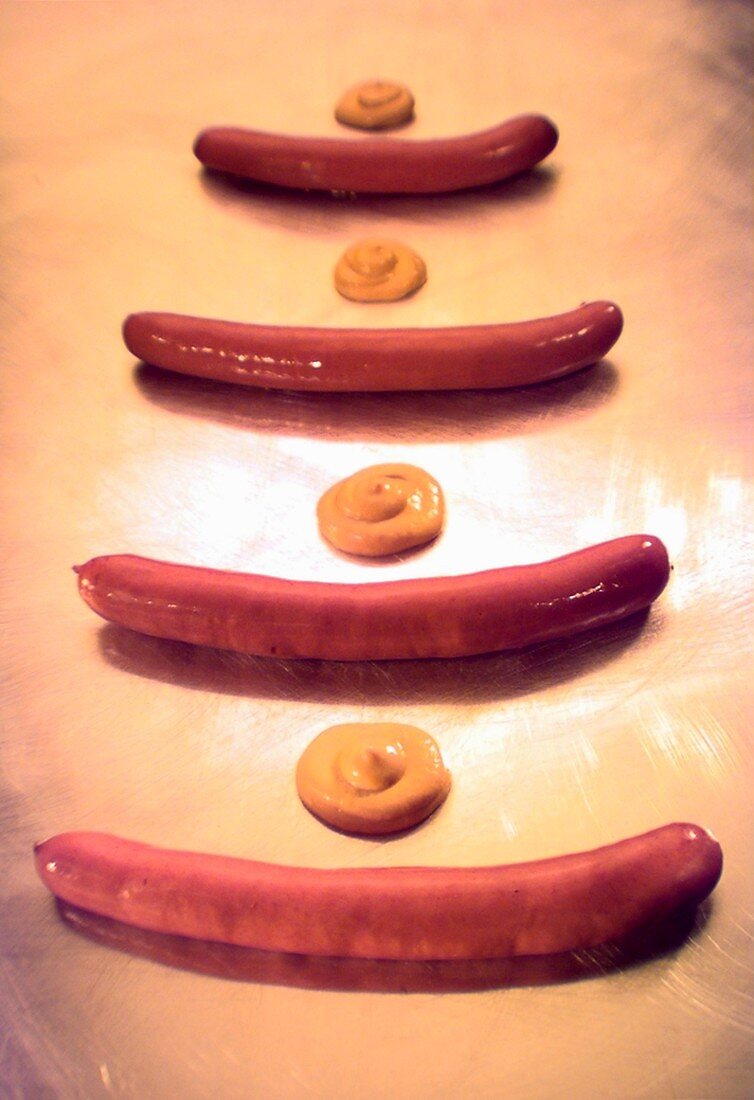 Four sausages with blobs of mustard, one behind the other