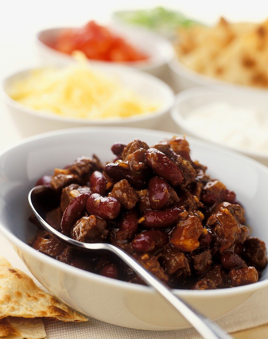 Chili con carne with various accompaniments behind