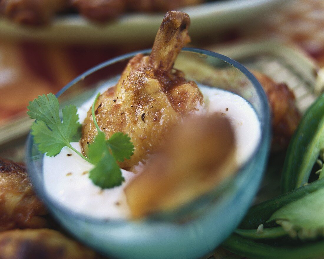 Barbecued chicken thighs in bowl with sour cream dip