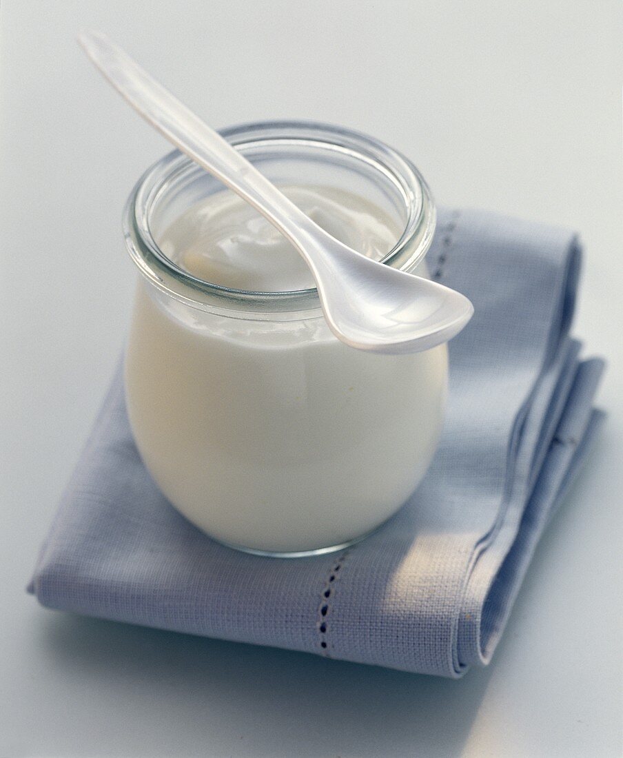 Ein Glas Joghurt mit Löffel auf hellblauem Tuch