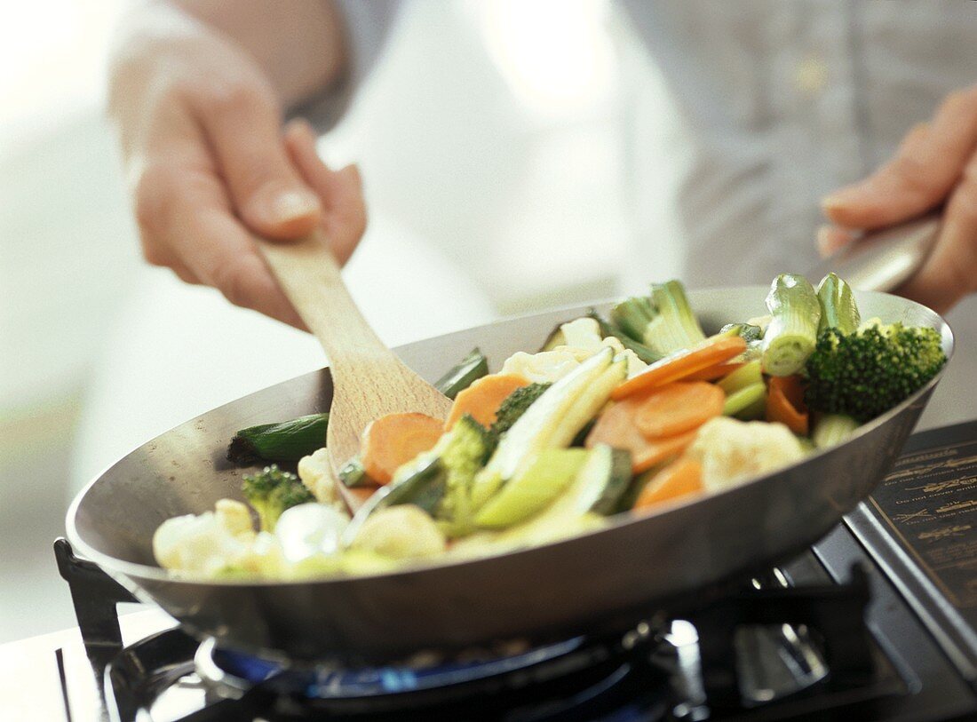 Stirring vegetable stir-fry on cooker