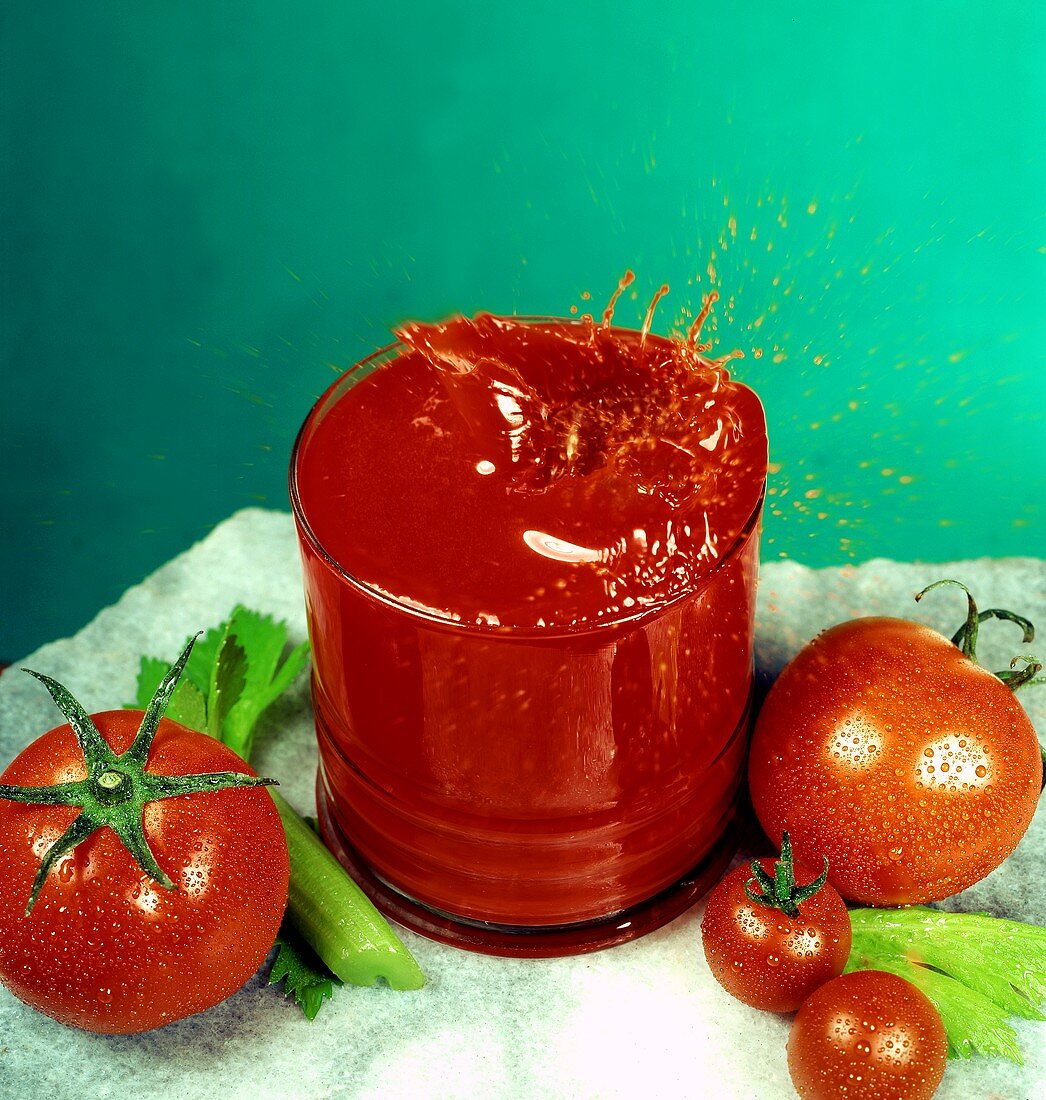 Tomatensaft spritzt aus dem Glas, daneben frische Tomaten