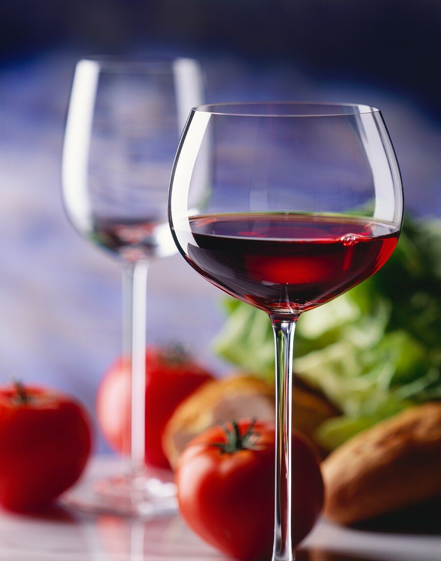Ein Glas junger Rotwein, dahinter Tomaten, Salat und Brot