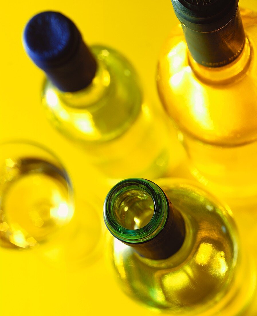 Drei Weissweinflaschen und ein Weinglas (von oben)