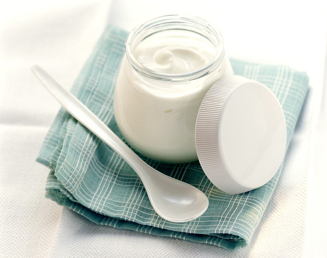 A jar of yoghurt with plastic spoon on pale-blue cloth