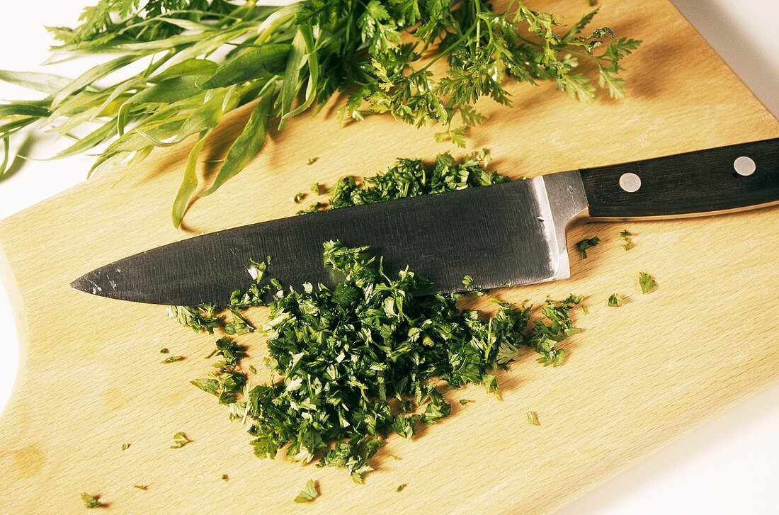 Freshly chopped herbs and chef's knife on chopping board