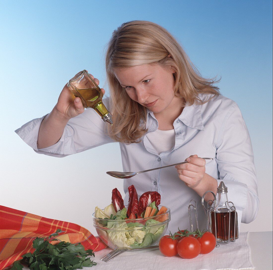 Young woman dressing mixed salad with oil