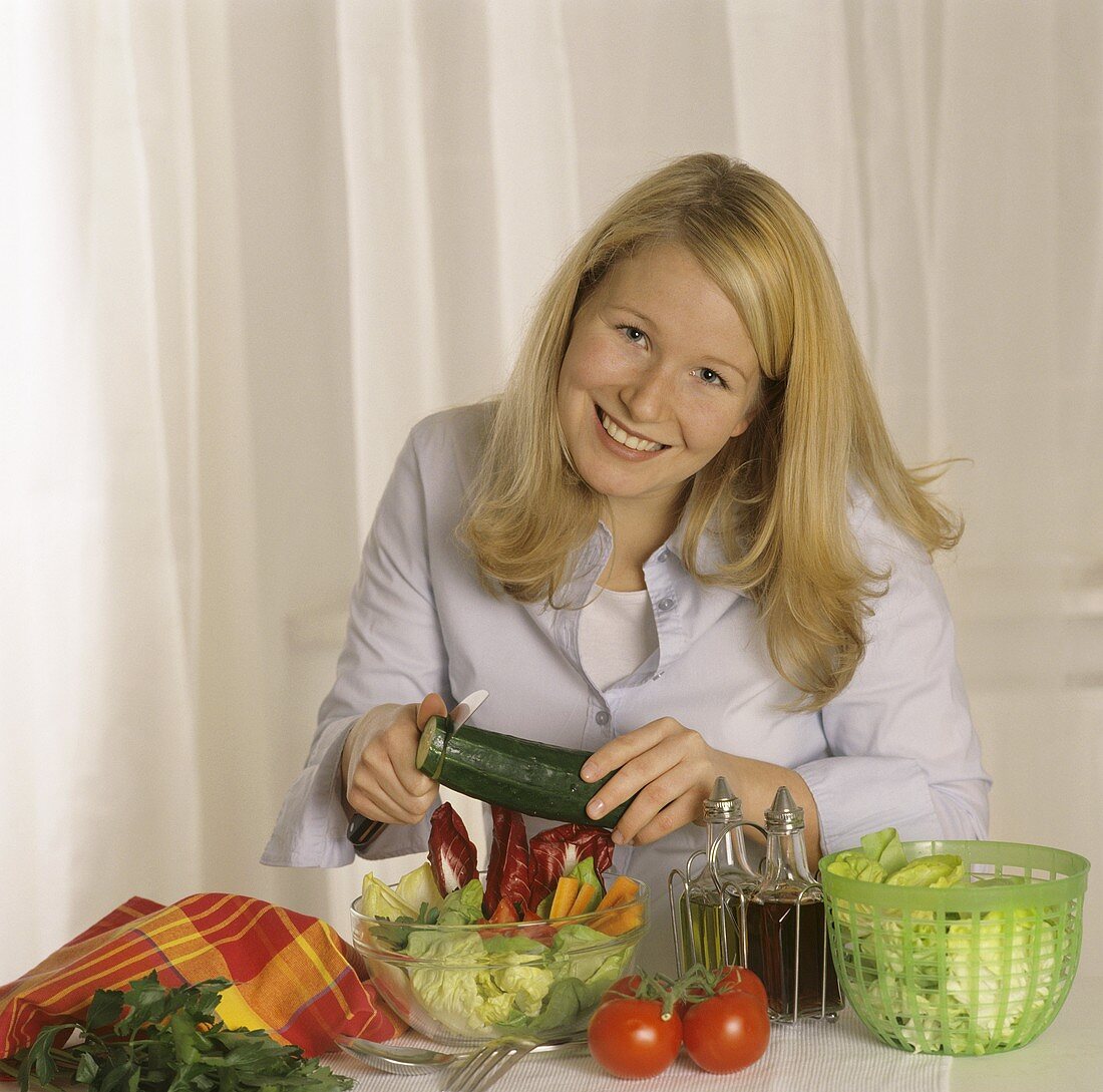 Young woman cutting cucumber into mixed salad