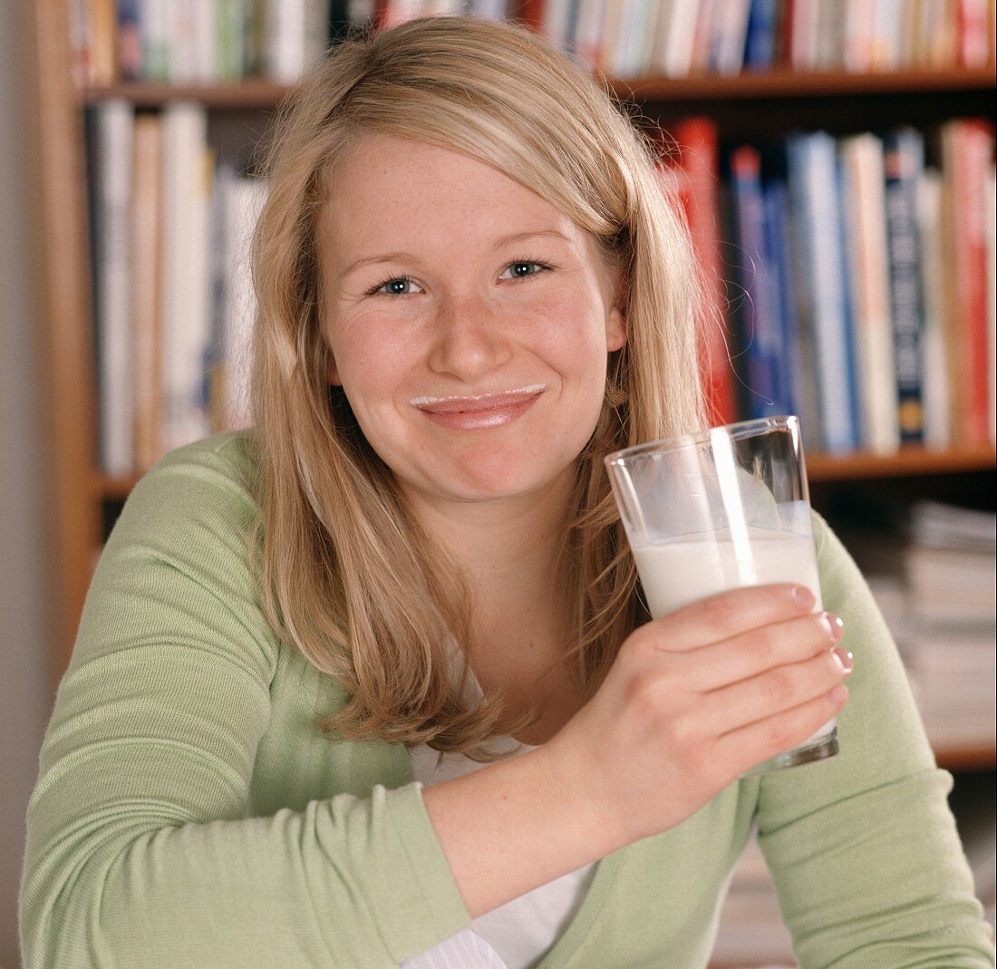 Blonde Frau mit einem Glas Milch und Milchrand am Mund