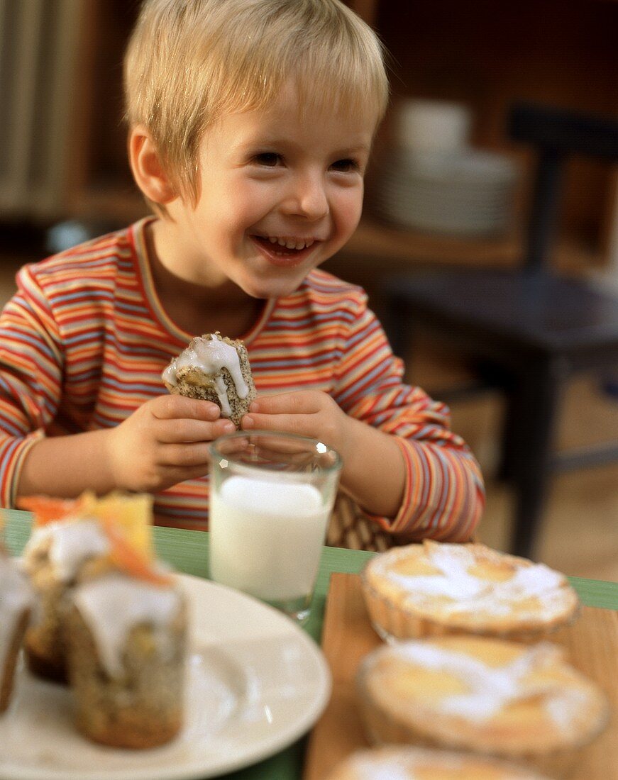 Kleiner Junge vor Tisch mit Gebäck und Milch hält Mohnmuffin