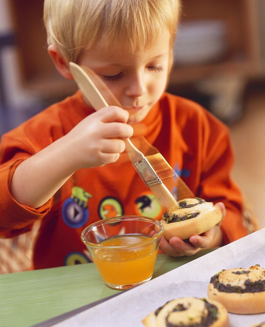 Small boy brushing poppy seed coil with apricot jam
