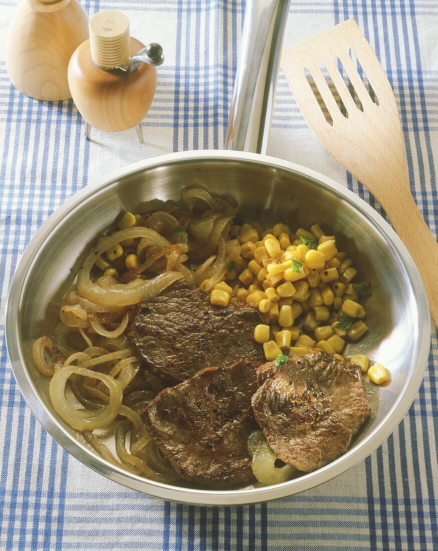 Beefsteaks with sweetcorn and onions in frying pan