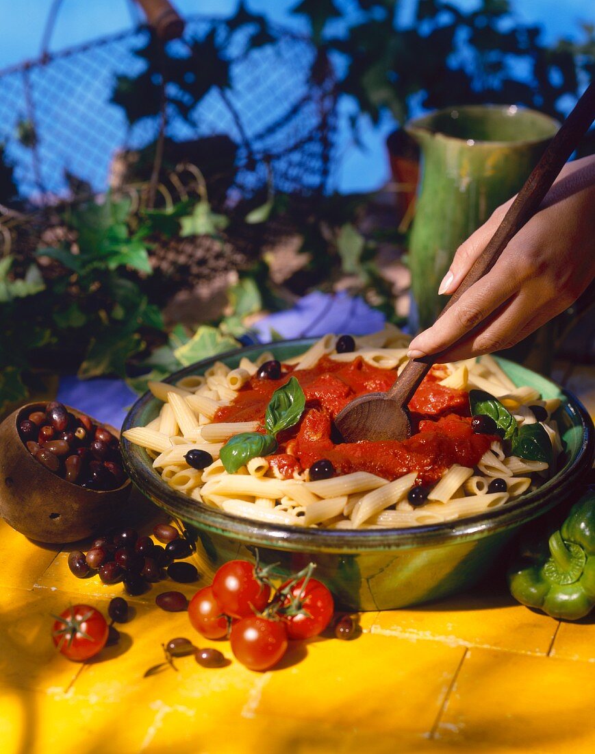 Penne with tomato sauce and olives being stirred 