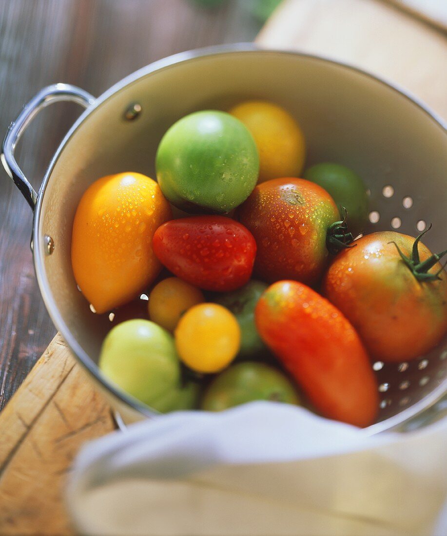 Tomatoes of various colours and sizes in metal strainer