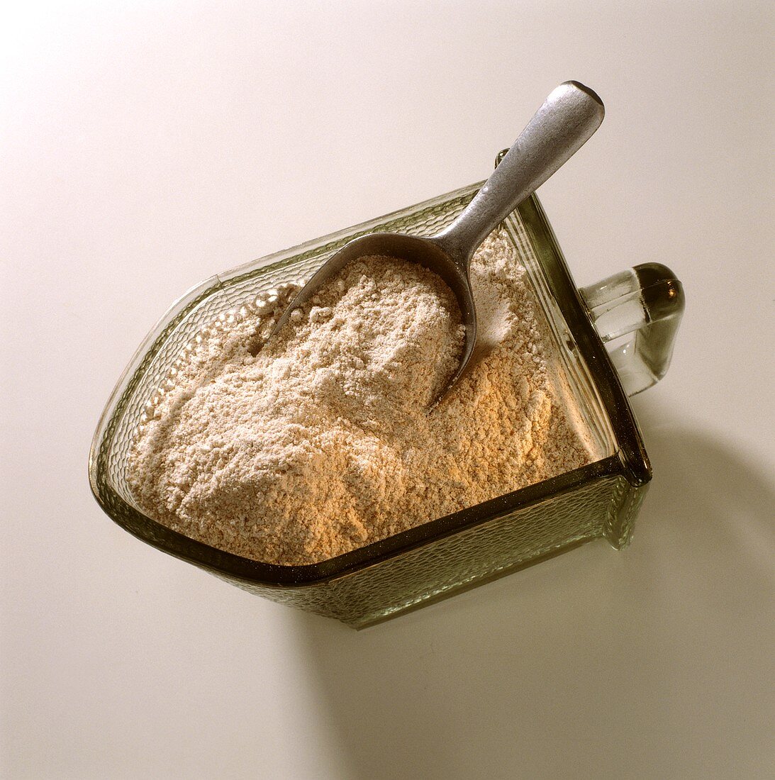 Wholemeal flour in glass container with small scoop