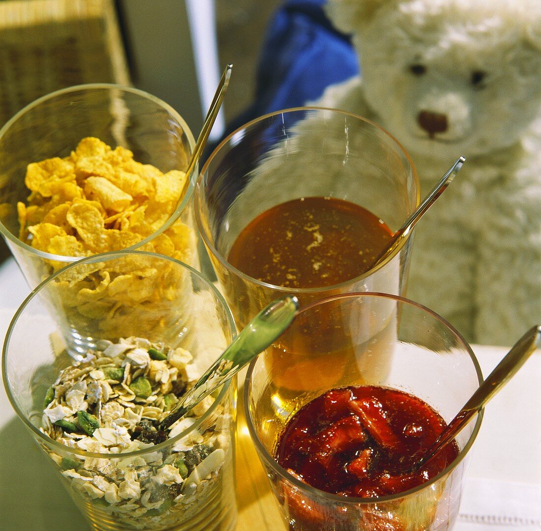 Muesli ingredients in glasses, teddy bear behind