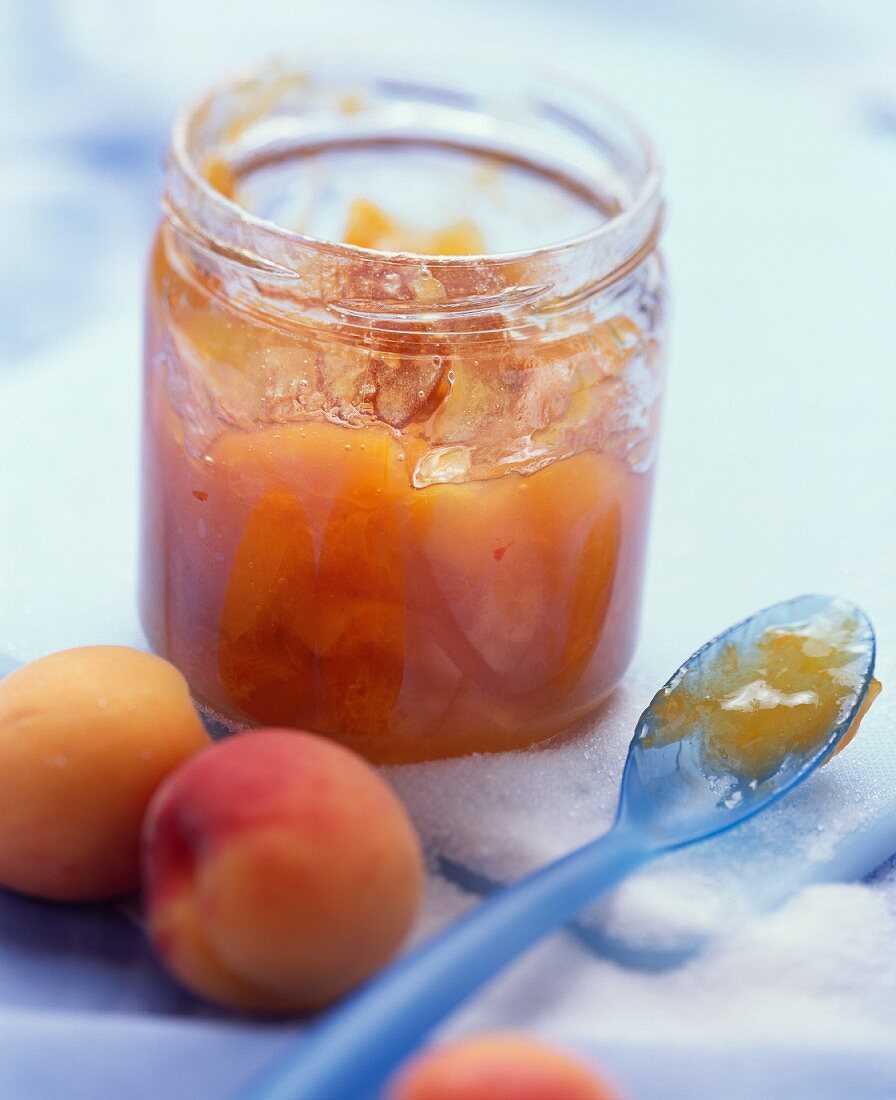 Aprikosenmarmelade im Glas, daneben Aprikosen und Zucker