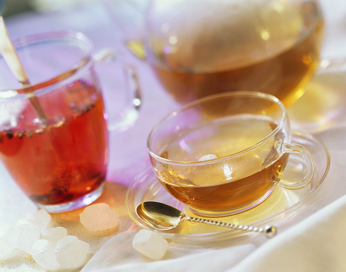 Eine Tasse Tee und ein Glas Früchtetee mit gläserner Teekanne