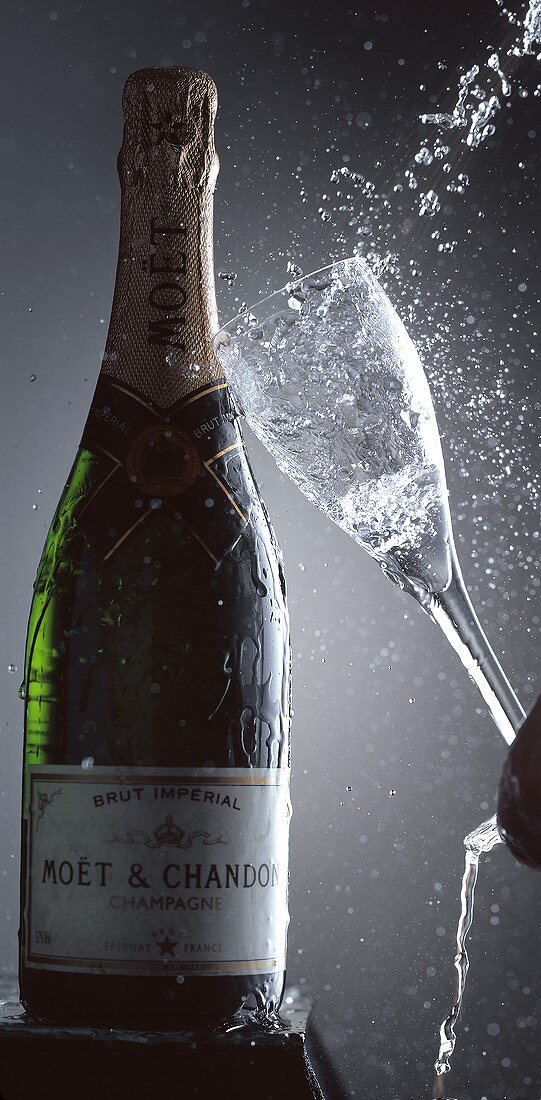 Sektglas fällt auf eine Flasche Champagner (Moet & Chandon)