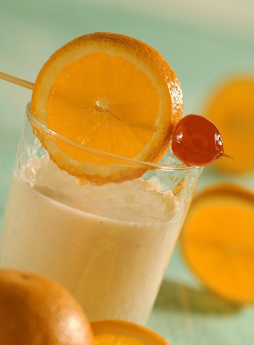Banana milkshake with slice of orange and cocktail cherry