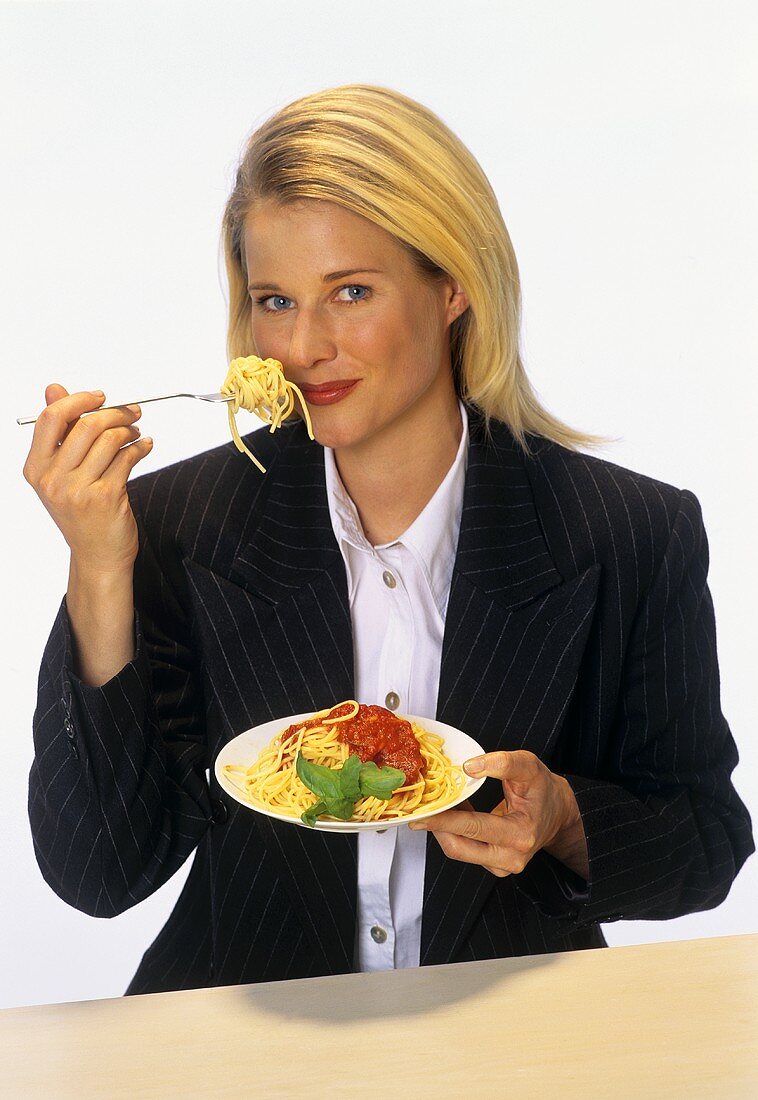 Young blond woman eating spaghetti with tomato sauce
